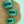 Three green and blue striped clips on a woven mat with a light blue background