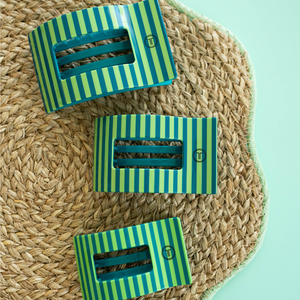 Three green and blue striped clips on a woven mat with a light blue background