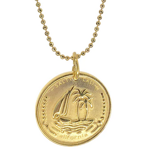 Gold necklace with a coin pendant featuring a sailboat and palm tree design on a white background