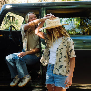 Woman helping a child put on a hat in the back of a black truck with a natural outdoor setting.