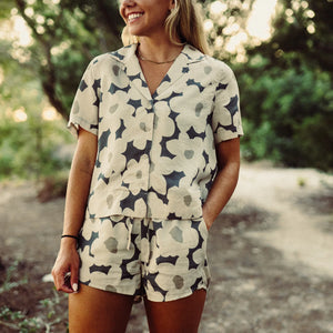 Woman wearing a floral patterned romper standing outdoors with greenery in the background