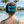 Person with a blue striped hair clip in their bun by a pool with palm trees and houses in the background