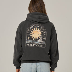 A woman viewed from the back wearing a dark charcoal gray hoodie with a large graphic print on the back. The graphic features a sun, stars, and the text 'IN REFUGE IN THE SKY' and 'SALTY CREW'.